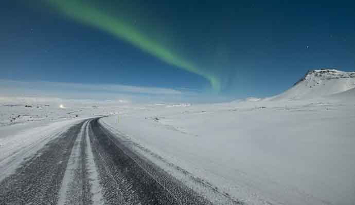 snowy road northern lights in distance