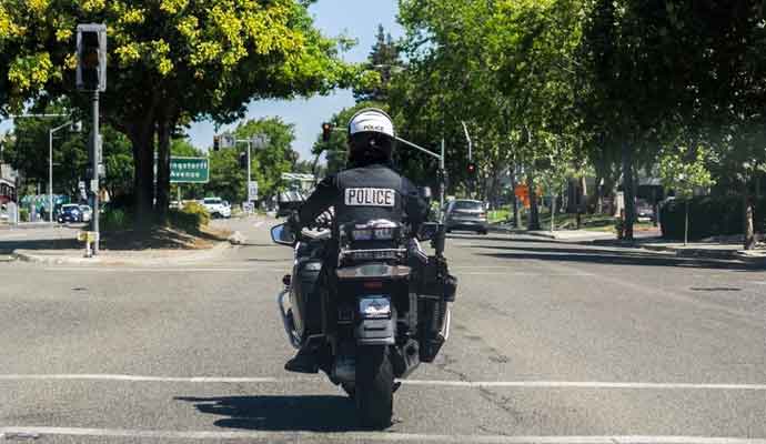 A motorcycle police officer on patrol on the streets of south San Francisco bay area; back view