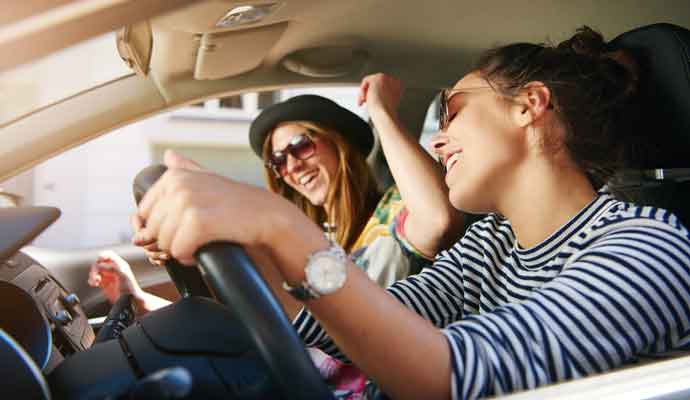 Two women singing along as they drive in the car through town