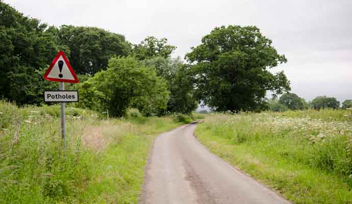 Same day courier companies on rural road with sign warning of potholes